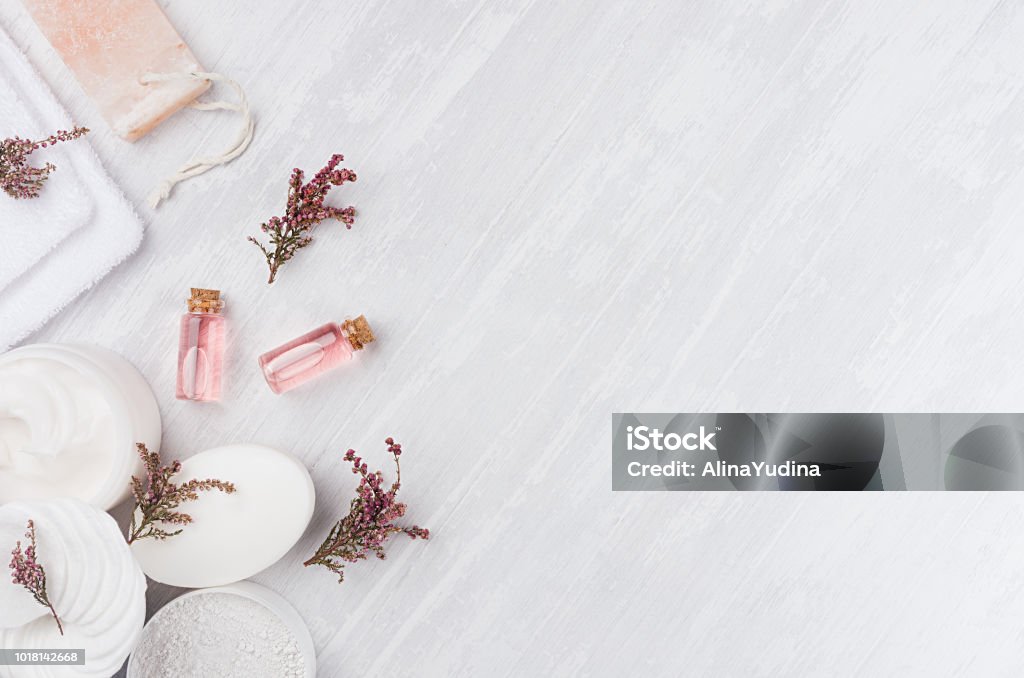 Organic homemade white cosmetics set with pink flowers and massage oil on white wooden board, top view, border. Backgrounds Stock Photo