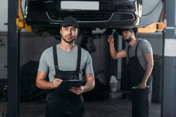 istock auto mechanic in overalls holding clipboard, while colleague working in workshop behind 1018158490