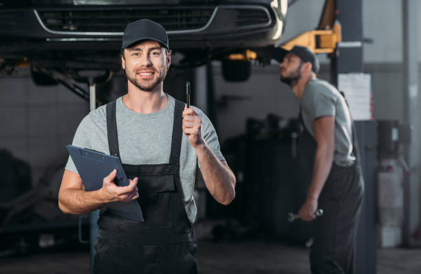 istock smiling mechanic wirh clipboard having idea, while colleague working in workshop behind 1018158576
