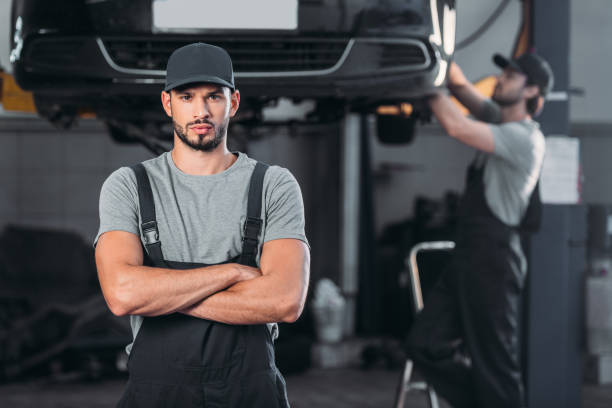 istock professional mechanic in overalls with crossed arms, while colleague working in workshop behind 1018158674