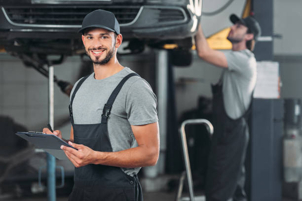 istock smiling mechanic writing in clipboard, while colleague working in workshop behind 1018158986