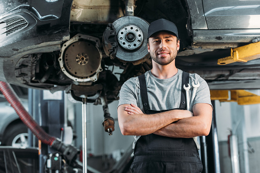sonriente trabajador posando con los brazos cruzados en el taller de mecánica de auto photo