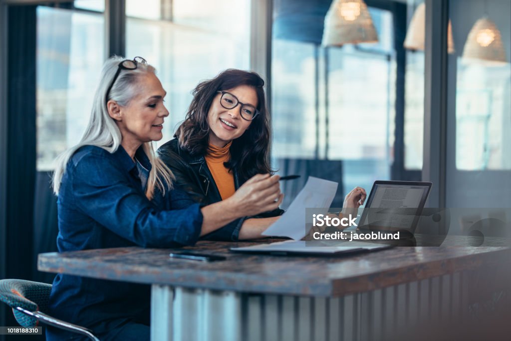 Two women analyzing documents at office Two women analyzing documents while sitting on a table in office. Woman executives at work in office discussing some paperwork. Discussion Stock Photo