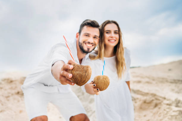 istock smiling young couple in white with coconut cocktails looking at camera 1018199074