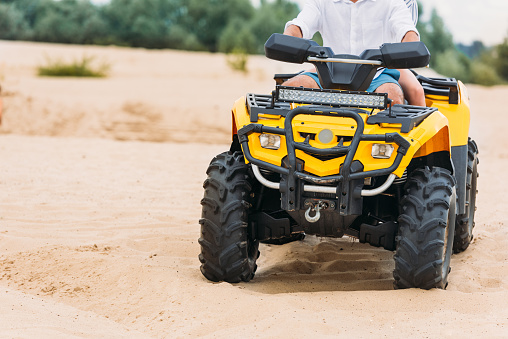 cropped shot of couple riding all-terrain vehicle on sand