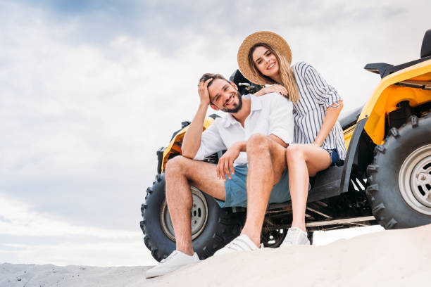 istock beautiful young couple sitting on ATV on sandy dune and looking at camera 1018199350