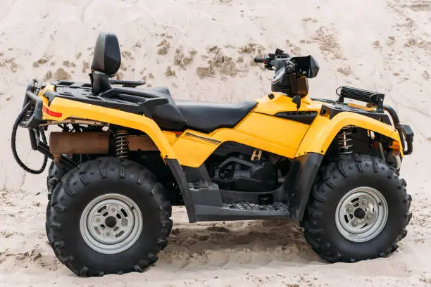 side view of modern yellow all-terrain vehicle standing in desert on cloudy day