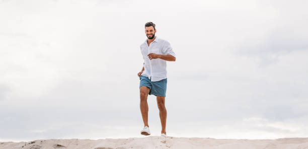 istock handsome young man running on sand dune in front of cloudy sky 1018199422