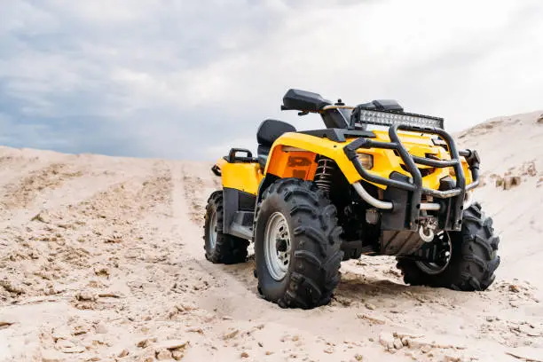 bottom view of modern yellow all-terrain vehicle standing in desert on cloudy day
