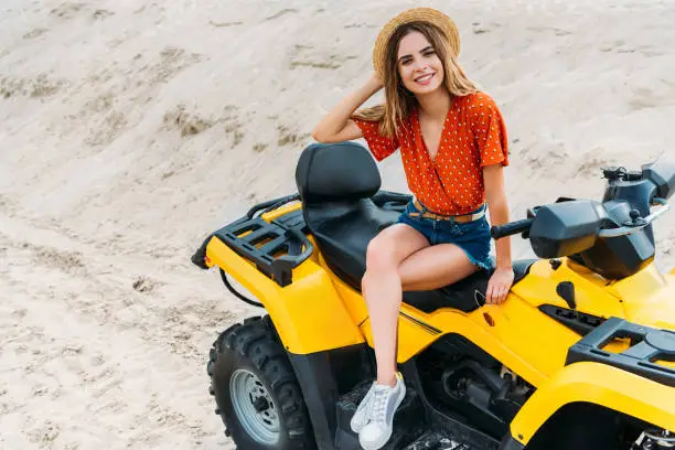 high angle view of happy young woman sitting on all-terrain vehicle on sand