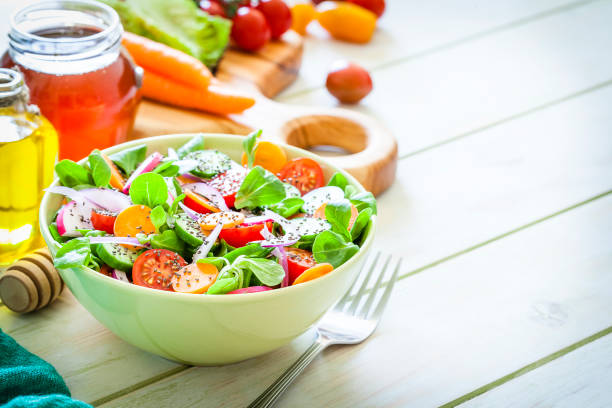 Green salad bowl filled with fresh organic colorful vegetables shot on light green picnic table. An olive oil bottle and a honey jar are beside the bowl. The composition is arranged at the left of an horizontal frame leaving useful copy space for text and/or logo. Vegetables included in the composition are tomatoes, cucumber, carrot, onion, arugula and lettuce. This ingredients are typical of the Mediterranean cuisine. High key DSRL studio photo taken with Canon EOS 5D Mk II and Canon EF 100mm f/2.8L Macro IS USM.