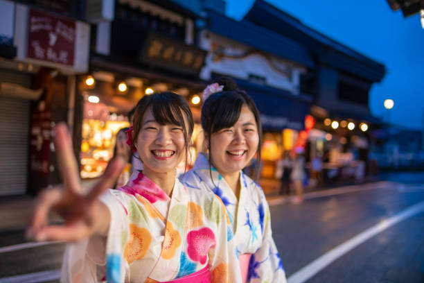 Young female friends in yukata smiling in traditional Japanese town Young female friends in yukata smiling in traditional Japanese town yukata photos stock pictures, royalty-free photos & images
