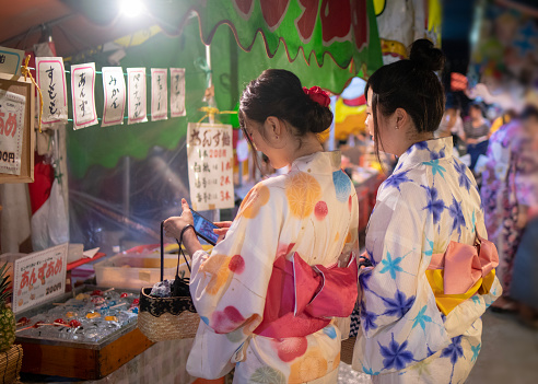 Young female friends in yukata shopping at Japanese Yatai market in festival