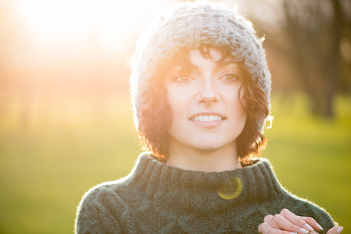 Backlit sunset portrait of young woman wearing a wooly hat and knitted sweater - autumn / winter outdoors shot with lots of real lens flare.