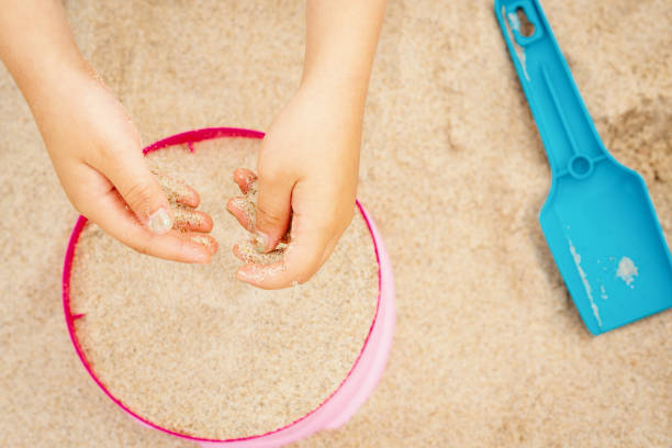 hands of a girl with sand over a colored bucket and shovel on the beach - sandbox child human hand sand imagens e fotografias de stock