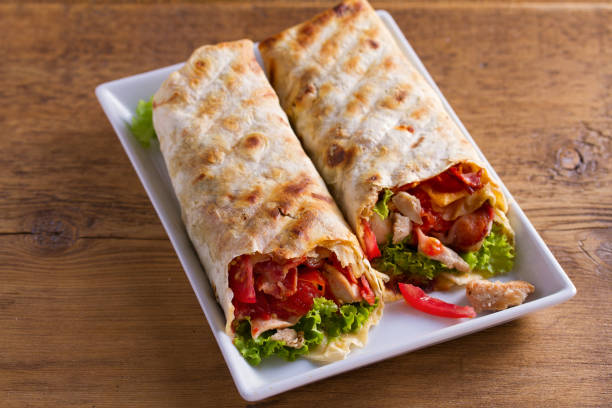 istock Chicken caesar salad wraps with bacon, tomatoes, lettuce and cheese. Tortilla, burritos, sandwiches twisted rolls 1018255224