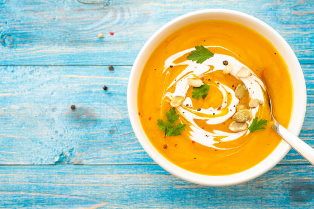 istock Pumpkin and carrot soup with parsley on blue background Top view. 1018260568
