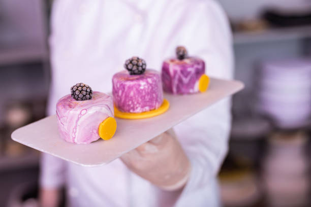 Plate with cakes. Chef wearing white gloves and jacket holding plate with blueberry cakes with mirror icing