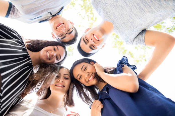 Friends standing in a circle outdoors Low angle view of group of teenagers standing in a huddle with their heads touching and looking at camera 16 17 years photos stock pictures, royalty-free photos & images