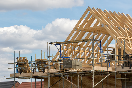 Construction industry. Timber framework of house roof trusses with scaffold on a building being built on a new housing estate.