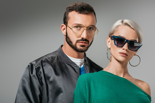 fashionable couple posing in eyeglasses and sunglasses, isolated on grey