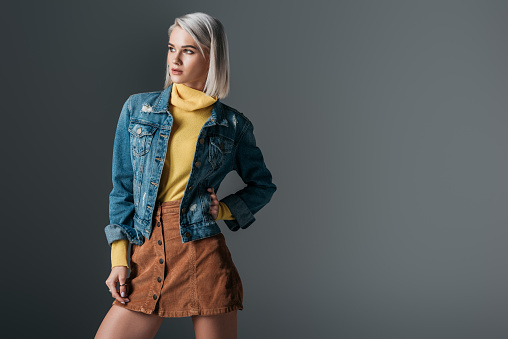 attractive woman posing in yellow turtleneck, trendy corduroy skirt and jeans jacket, isolated on grey