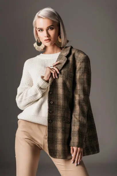 Photo of elegant woman posing in white sweater and autumn tweed jacket, on grey