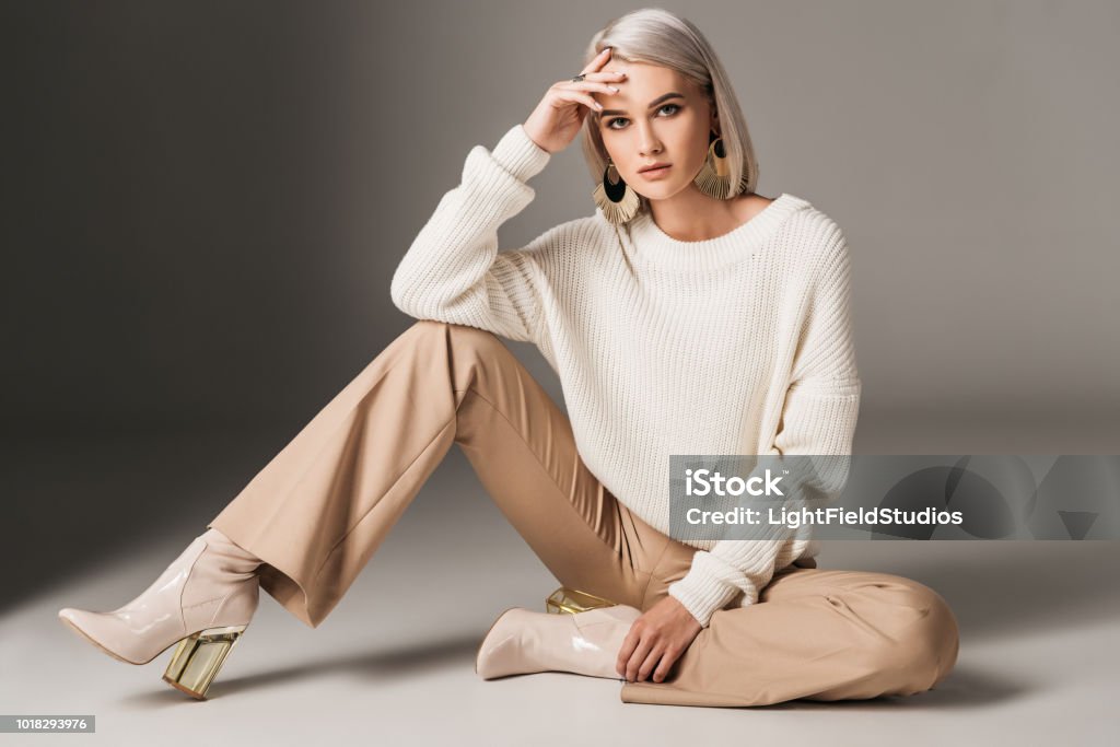 attractive fashionable woman posing in white trendy sweater, beige pants and autumn heels, on grey Fashion Stock Photo