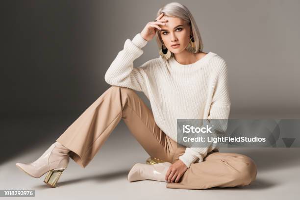 Attractive Fashionable Woman Posing In White Trendy Sweater Beige Pants And Autumn Heels On Grey Stock Photo - Download Image Now