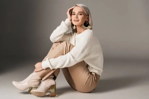 Photo of elegant fashionable woman posing in white sweater and autumn heels, on grey