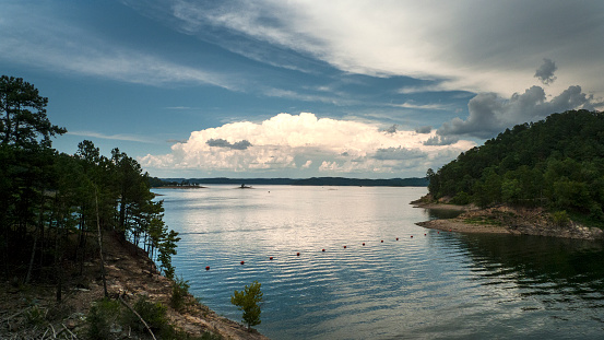 Summer storm clouds over a large, still water lake with mountains on the horizon. Scenic area of southeastern Oklahoma. Blue skies and storm clouds approaching.