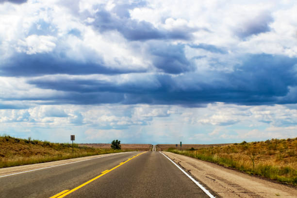 istock Road trip -Two lane highway on the plains stretches straight over horizonunder dramatic sky with strange light 1018302094