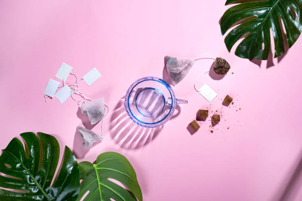 istock Top view, office table desk with copy space. Workspace frame with green tropical leaf and tea cup, tea bag and sugar on pastel pink background with beautiful deep shadows. Flay lay. 1018302206