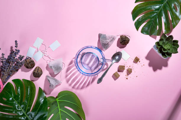 istock Top view, office table desk with copy space. Workspace frame with green tropical leaf and tea cup, tea bag and sugar on pastel pink background with beautiful deep shadows. Flay lay. 1018302238