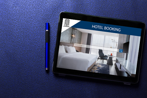 Hotel booking app concept on tablet screen with blue pen on blue pattern textured background