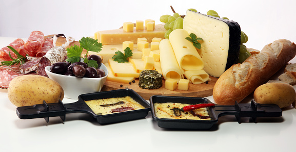Delicious traditional Swiss melted raclette cheese on diced boiled or baked potato served in individual skillets with salami.