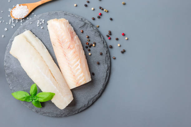 Fresh raw cod fillet with spices, pepper, salt, basil on stone plate, horizontal, copy space, top view stock photo