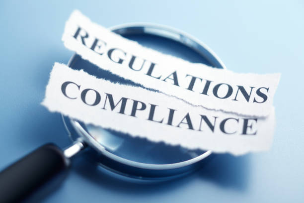 Compliance And Regualtion Concept The words "Compliance" and "Regulations" are printed on a torn pieces of paper that sit on top of a magnifying glass which sits on a blue background. The image is created using a very shallow depth of field. rules photos stock pictures, royalty-free photos & images