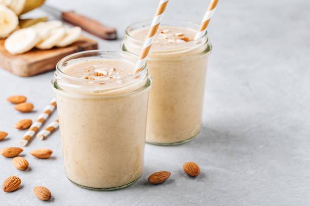 smoothie banane amande avec des flocons d’avoine et de la cannelle et le lait de coco en bocaux de verre - aliment battu photos et images de collection