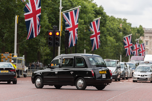 London, UK - Jul 25, 2017: Large British flags on The Mall Street early in the day as a black cab turns a corner.
