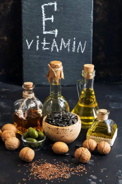 Photo of Food rich in vitamin E on a black concrete background. Oil, seeds, nuts. Selective focus, sign with text.