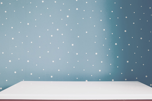 Empty white table and soft grey blue starry wall in kids room.
