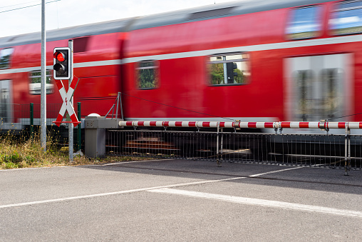 A passenger train passing through a guarded railway crossing with closed barriers and a red light.