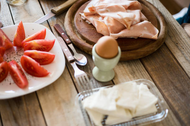 Breakfast - Hands holding and tearing bread slice. Mortadella, boiled egg, soft cheese and tomato slices in background