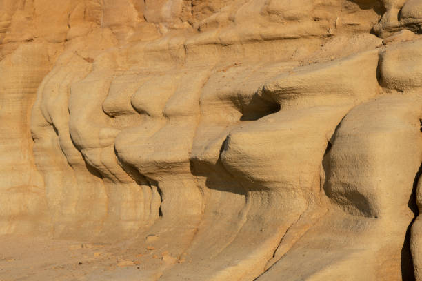 The red, orange and yellow sand stone cliffs of a rocky shore or beach on the Greek Island of Chios in the Aegean Sea in the golden morning light in summer. Shallow depth of field with focus placed over the nearest parts large rocks (formation). Many refugees travelling from Turkey to Greece have landed on this particular beach.