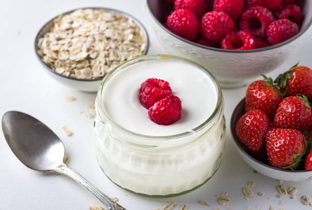 istock White yogurt in glass bowl with spoon and starwberries on white background. 1018433128