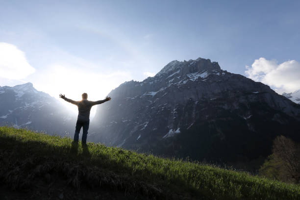 istock Man walks into meadow, below towering mountains 1018439610