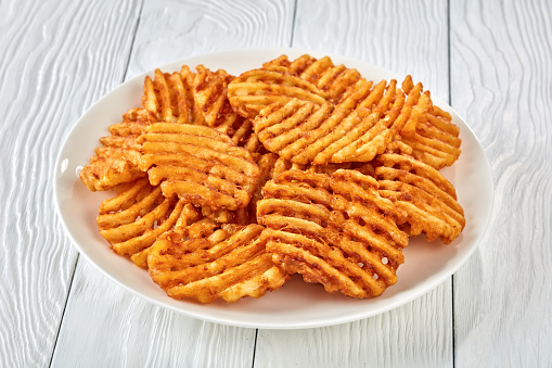 Crispy Potato Waffles Fries, Wavy, Crinkle Cut, Criss Cross Fries on a white plate on a wooden table, view from above, close-up