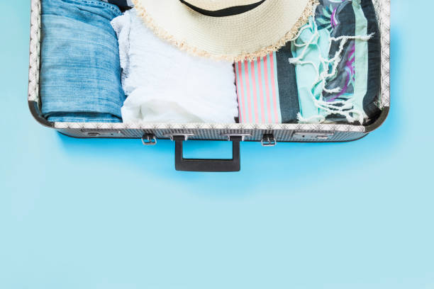 istock Open suitcase with female clothes for trip on pastel blue. Top view with copy space. Summer concept travel. 1018446390