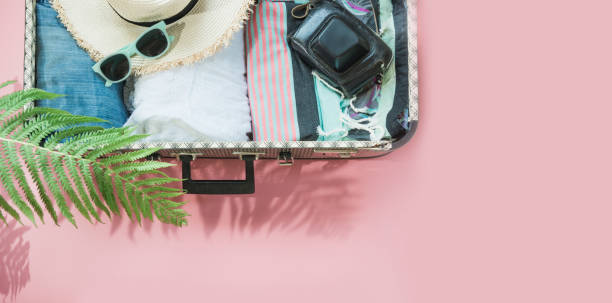 istock Open suitcase with female clothes for trip on pastel pink. Top view with copy space. Summer concept travel. 1018446404